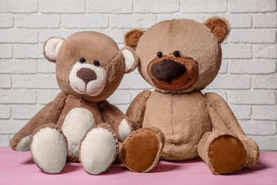 Photo of Cute teddy bears on pink wooden table near white brick wall