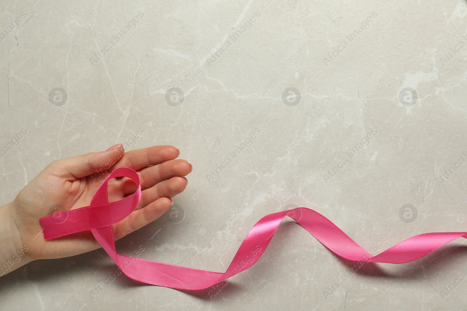 Photo of Breast cancer awareness. Woman with pink ribbon at light grey table, top view. Space for text