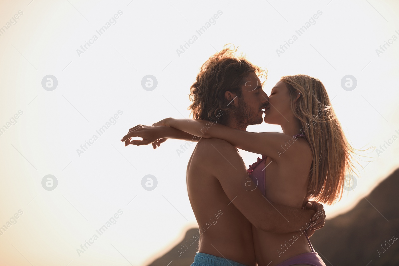 Photo of Young woman in bikini kissing her boyfriend on beach at sunset. Lovely couple