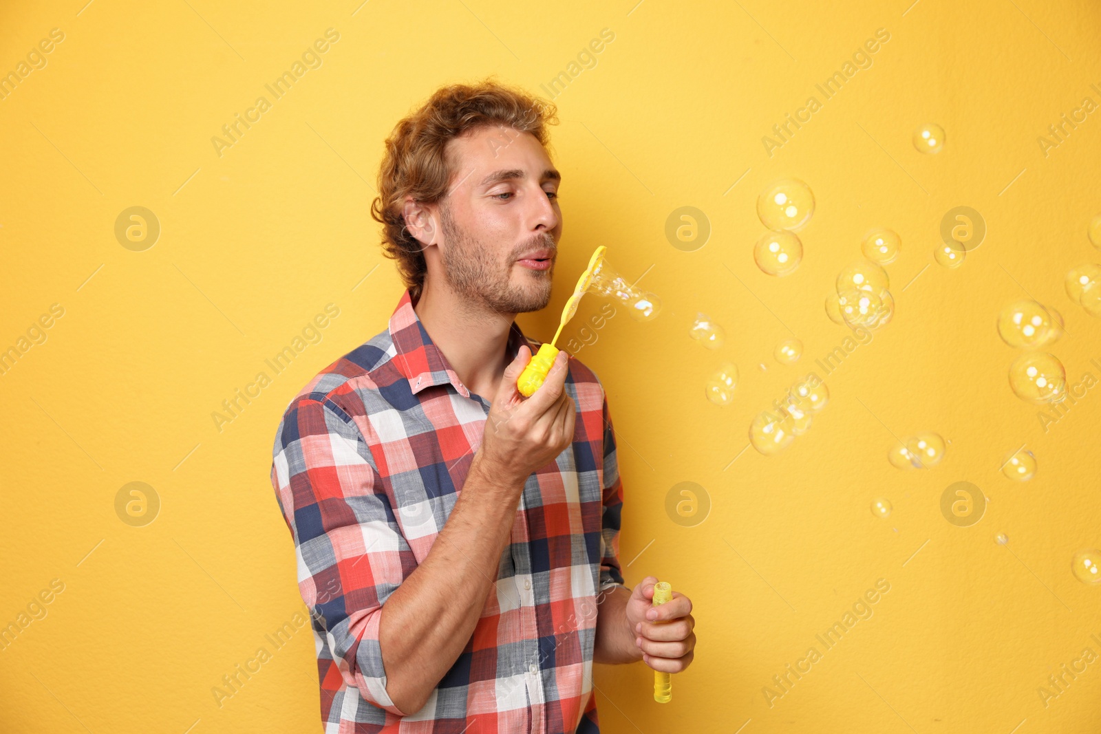 Photo of Young man blowing soap bubbles on color background