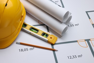 Rolled construction drawings, safety hat, pencil and bubble level on house plan. Architect workspace