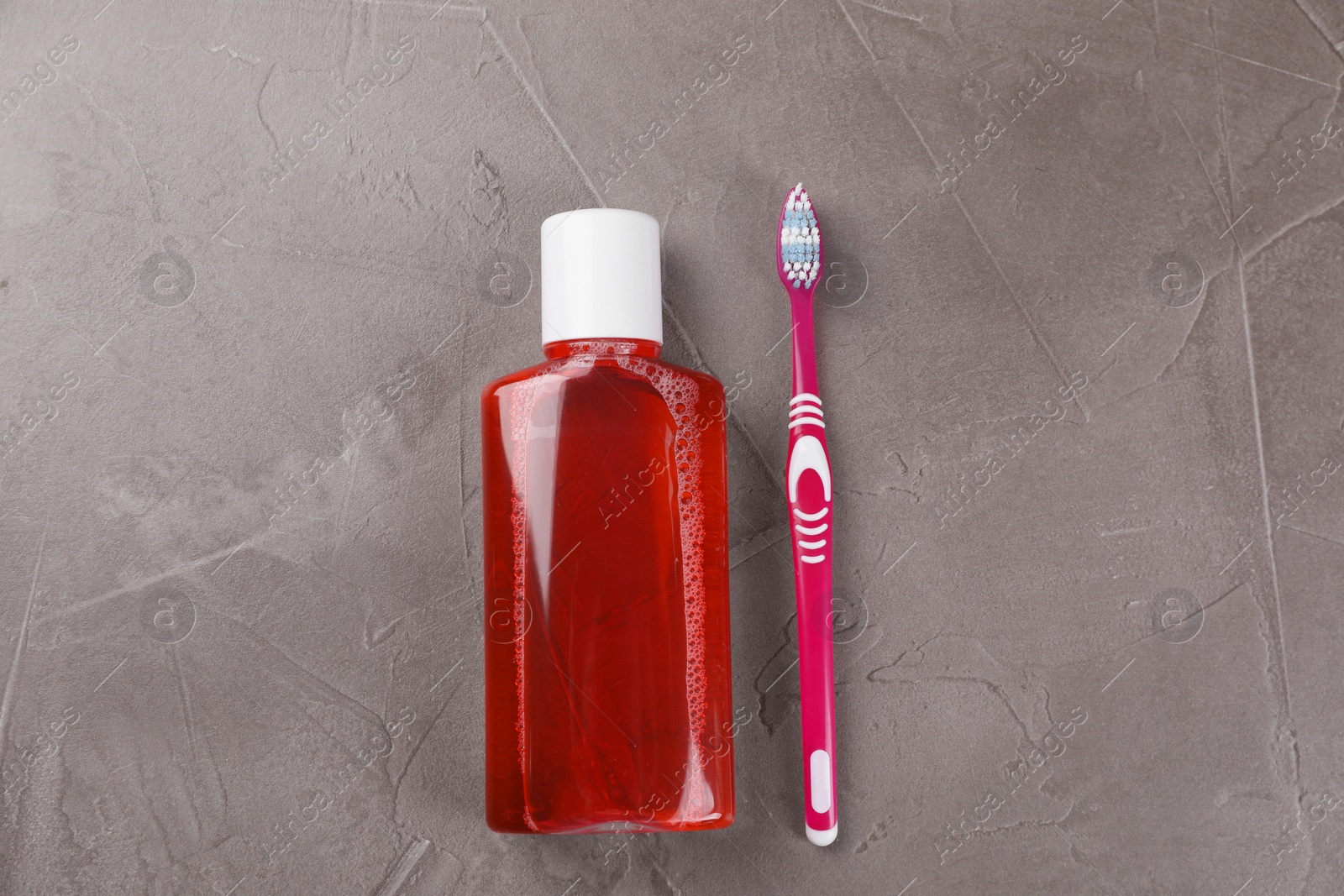 Photo of Fresh mouthwash in bottle and toothbrush on grey textured table, top view