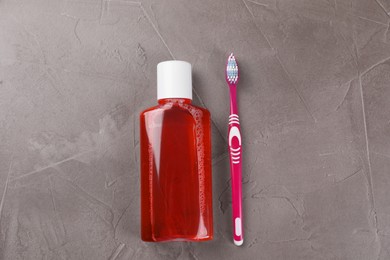 Photo of Fresh mouthwash in bottle and toothbrush on grey textured table, top view