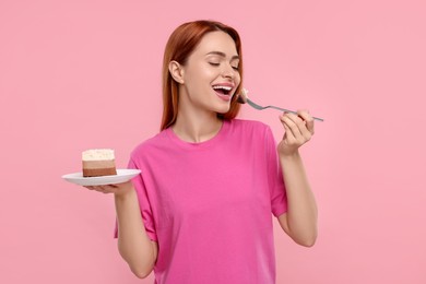 Young woman eating piece of tasty cake on pink background