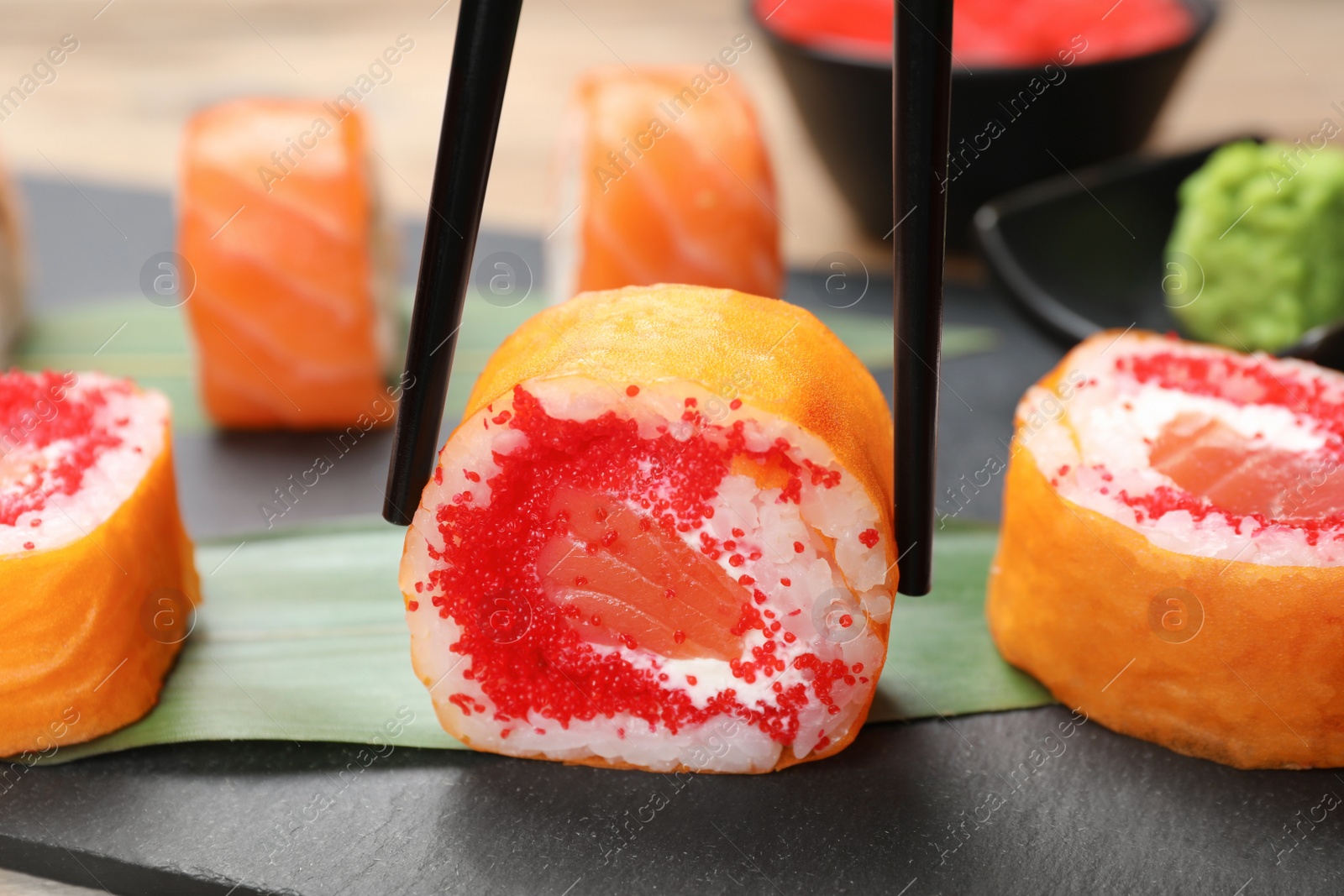 Photo of Taking delicious sushi roll with chopsticks at table, closeup