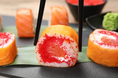 Photo of Taking delicious sushi roll with chopsticks at table, closeup