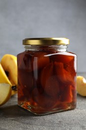 Photo of Tasty homemade quince jam in jar and fruits on grey textured table, closeup