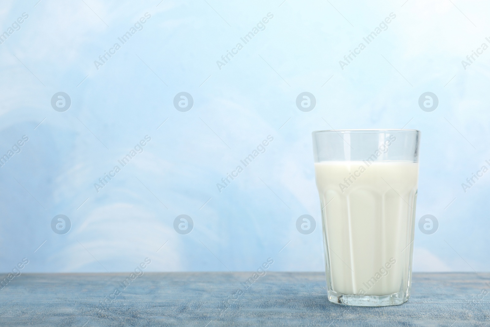 Photo of Glass with fresh milk on table against color background. Space for text