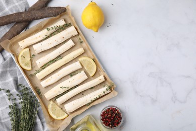 Baking tray with raw salsify roots, lemon and thyme on white marble table, flat lay. Space for text