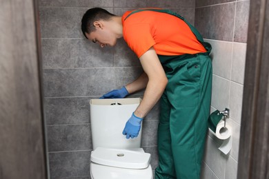 Young plumber repairing toilet bowl in water closet