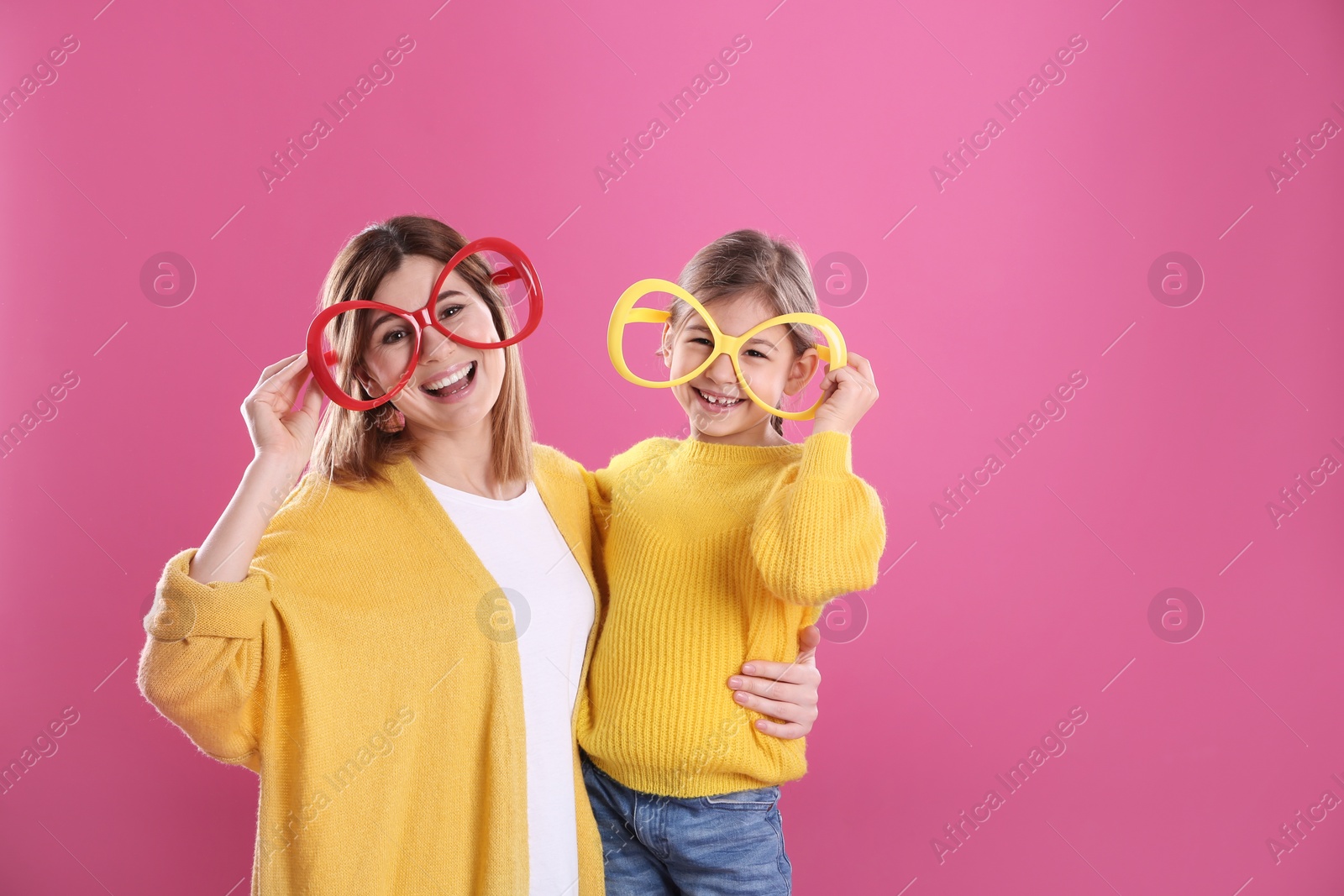 Photo of Happy woman and daughter with funny glasses on color background. Space for text