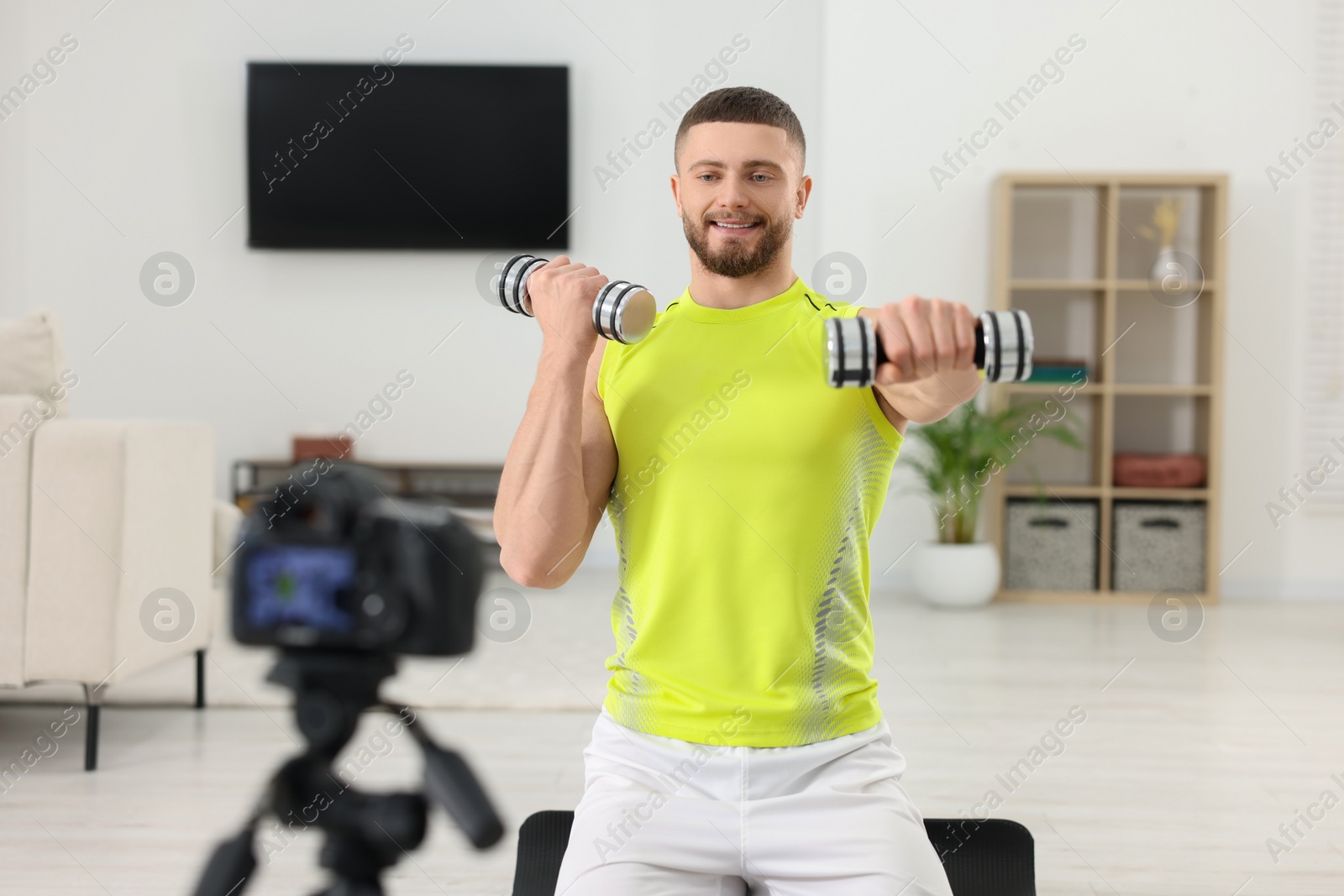 Photo of Trainer with dumbbells recording workout on camera at home