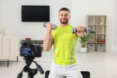 Photo of Trainer with dumbbells recording workout on camera at home