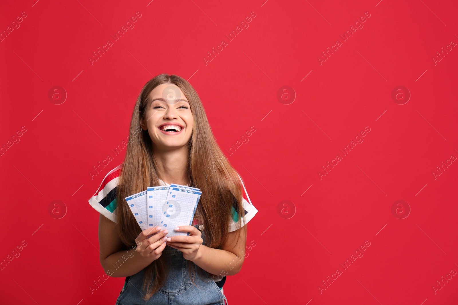 Photo of Portrait of happy young woman with lottery tickets on red background