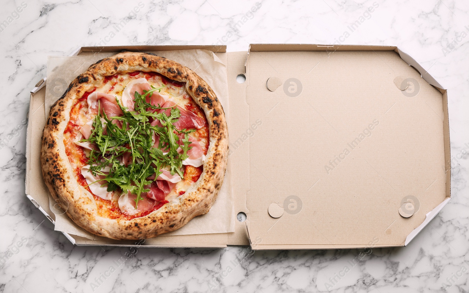 Photo of Tasty pizza with meat and arugula in cardboard box on white marble table, top view