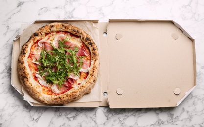 Photo of Tasty pizza with meat and arugula in cardboard box on white marble table, top view