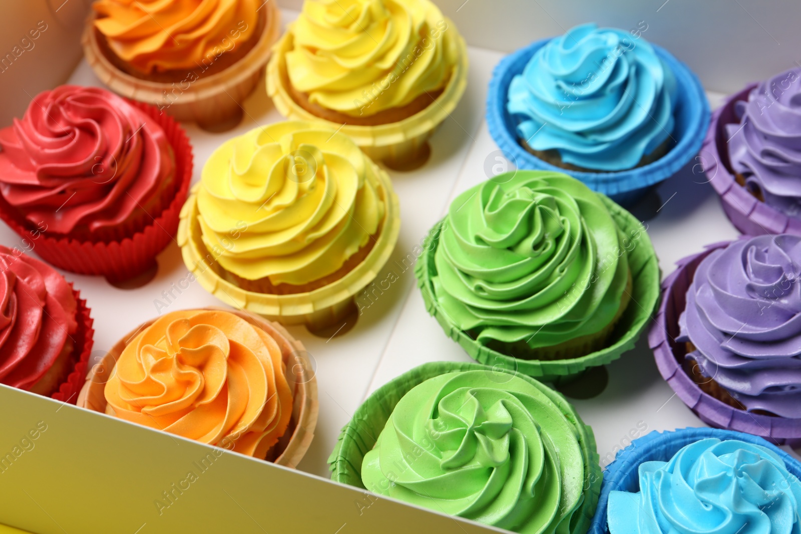 Photo of Many tasty cupcakes with colorful cream in box, closeup