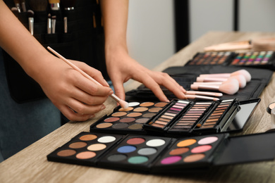Photo of Professional makeup artist with brush and eyeshadow palette at wooden table indoors, closeup