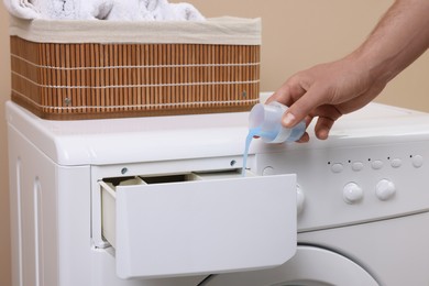 Man pouring fabric softener from cap into washing machine indoors, closeup