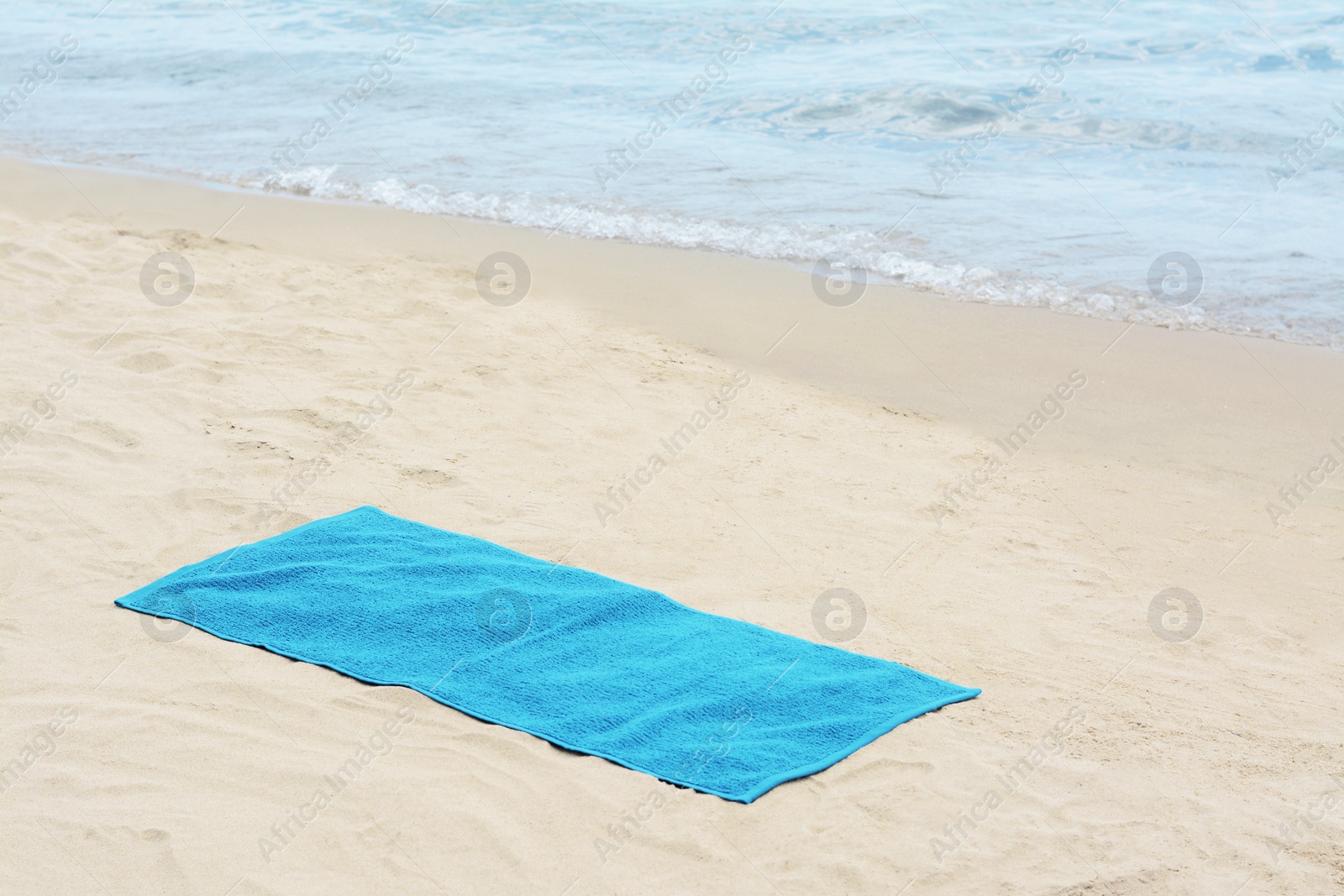 Photo of Blue towel on sandy beach near sea, space for text