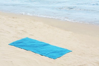 Blue towel on sandy beach near sea, space for text