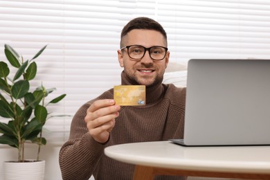 Photo of Handsome man with credit card using laptop for online shopping at home