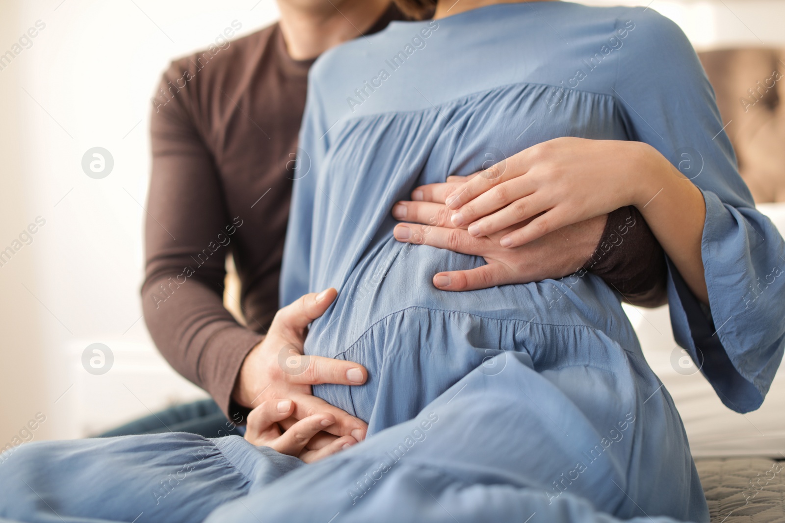 Photo of Pregnant couple sitting on bed at home, closeup