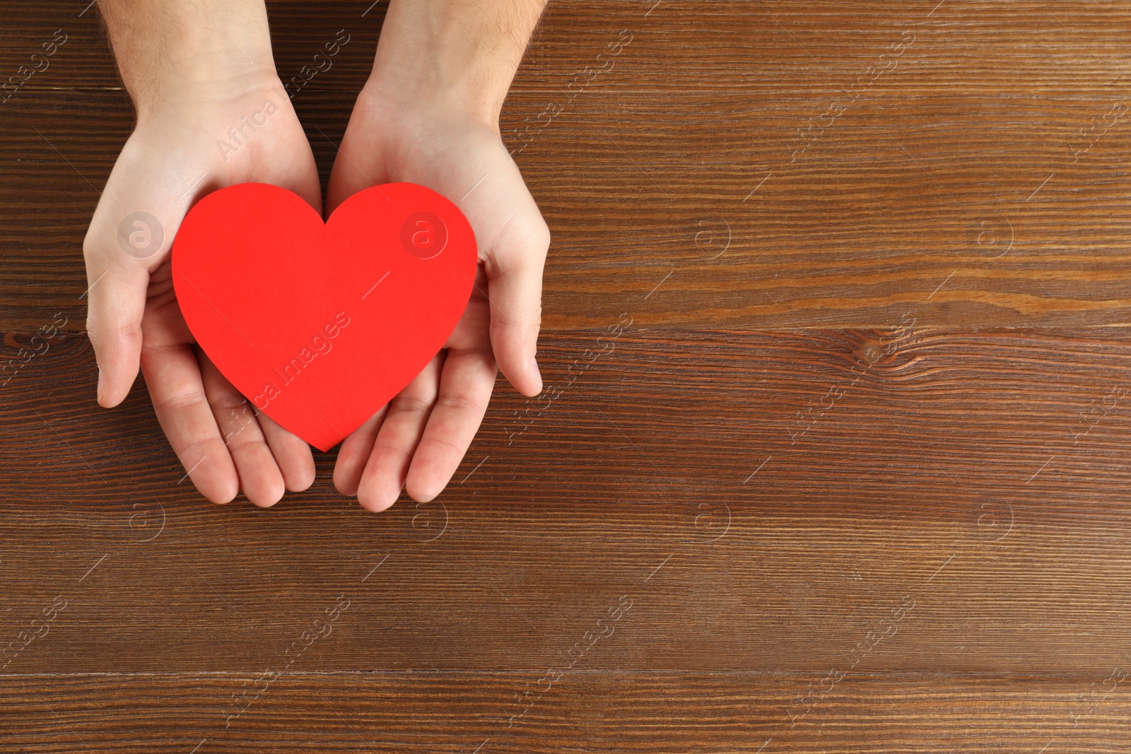 Photo of Man holding paper heart on wooden background, top view with space for text