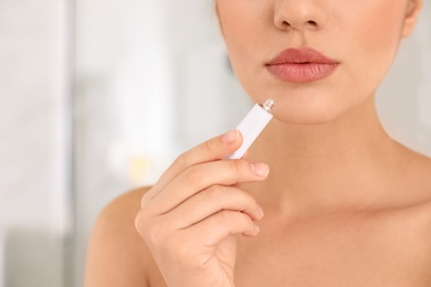 Photo of Woman with herpes applying cream on lips against blurred background, closeup