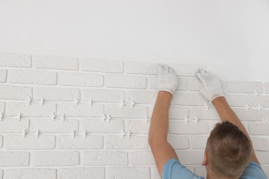 Photo of Professional builder installing new white decorative bricks on wall, closeup