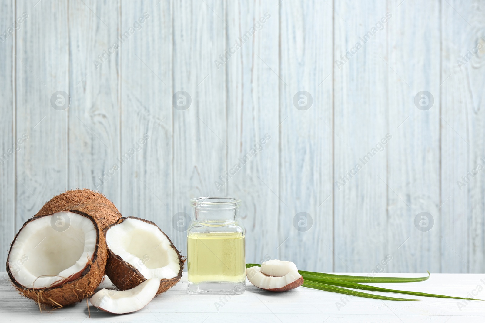 Photo of Jar of natural organic oil and coconuts on white wooden table. Space for text