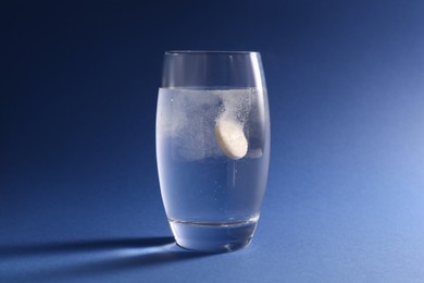 Photo of Effervescent pill dissolving in glass of water on blue background