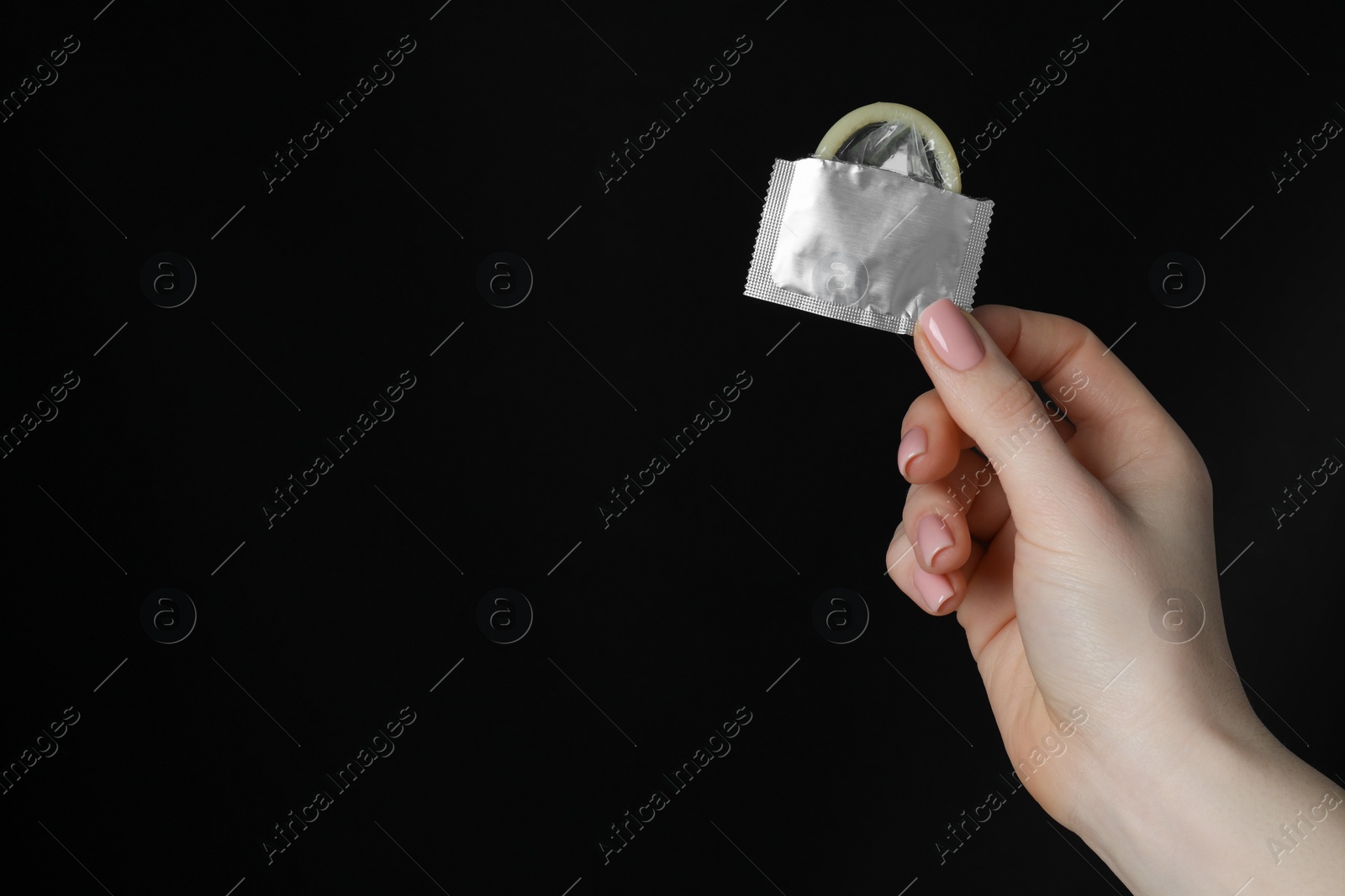 Photo of Woman holding condom on black background, closeup. Space for text