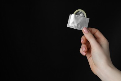 Photo of Woman holding condom on black background, closeup. Space for text