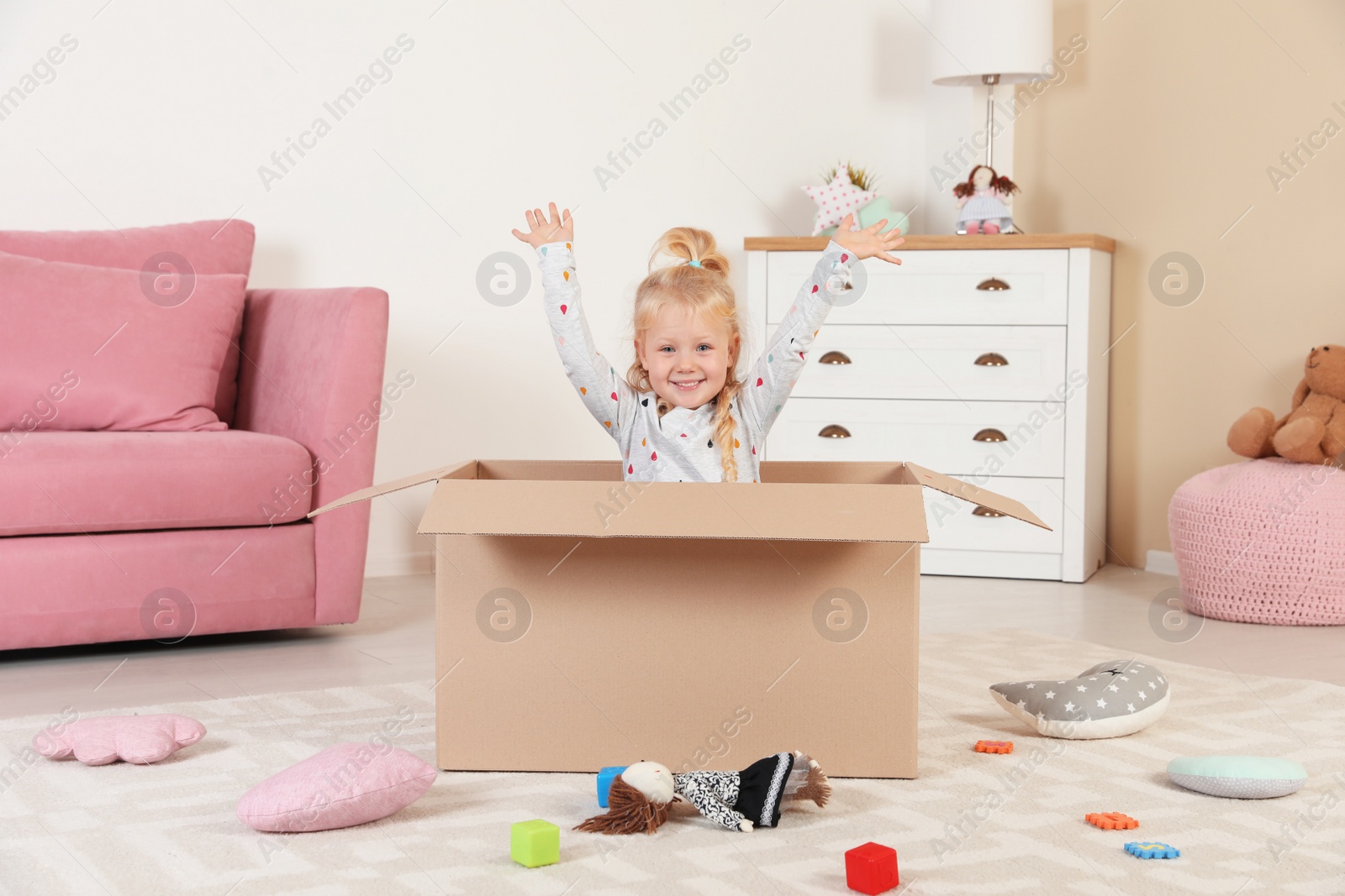 Photo of Cute little girl playing with cardboard box at home