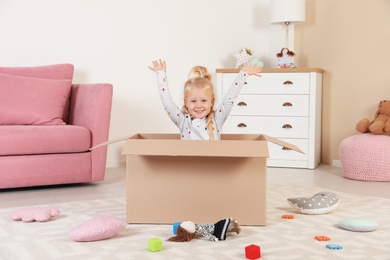 Cute little girl playing with cardboard box at home