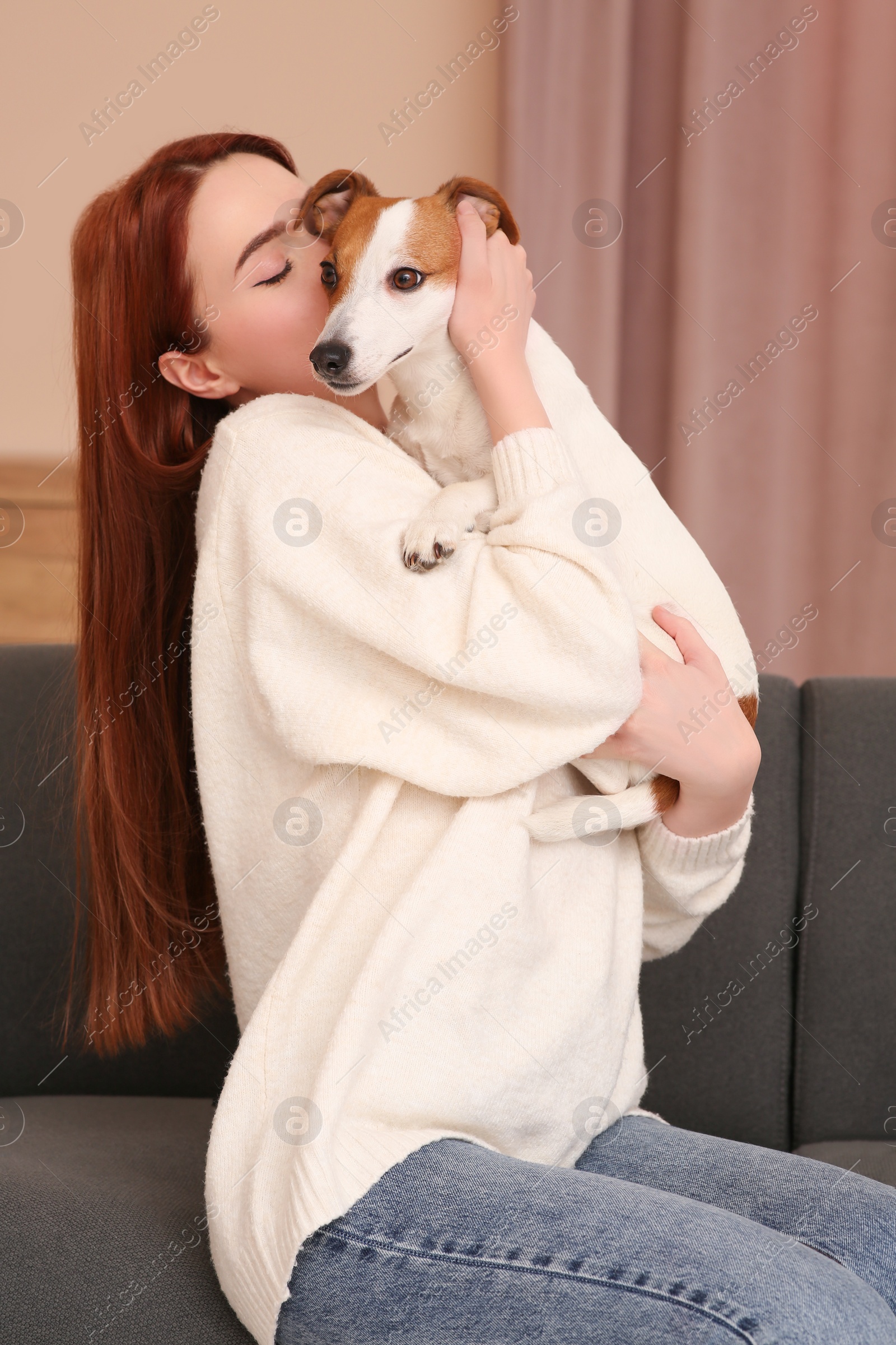 Photo of Woman kissing cute Jack Russell Terrier dog on sofa at home