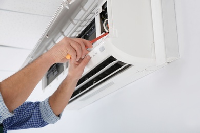 Electrician with screwdriver repairing air conditioner indoors, closeup