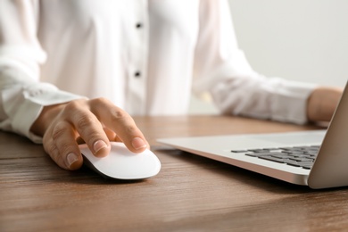 Woman using computer mouse with laptop at table, closeup