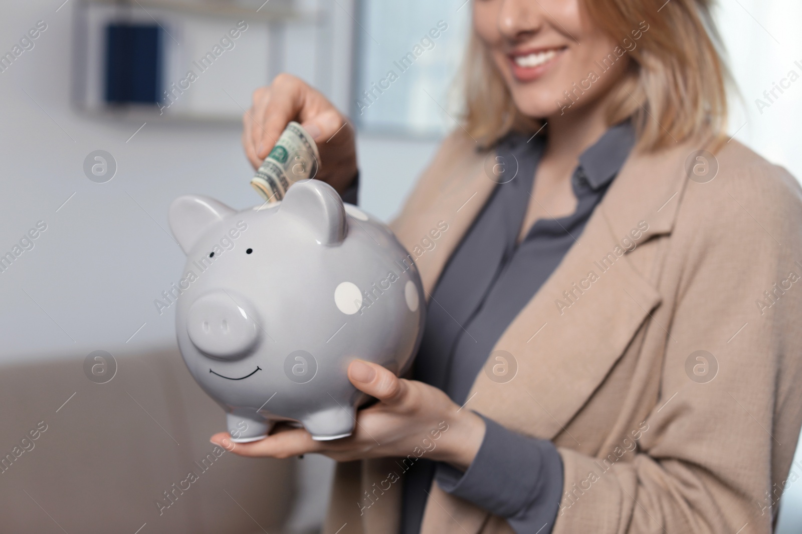 Photo of Businesswoman putting money into piggy bank indoors, closeup