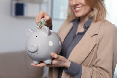 Businesswoman putting money into piggy bank indoors, closeup