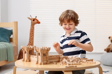 Cute little boy playing with wooden construction set at table in room. Child's toy