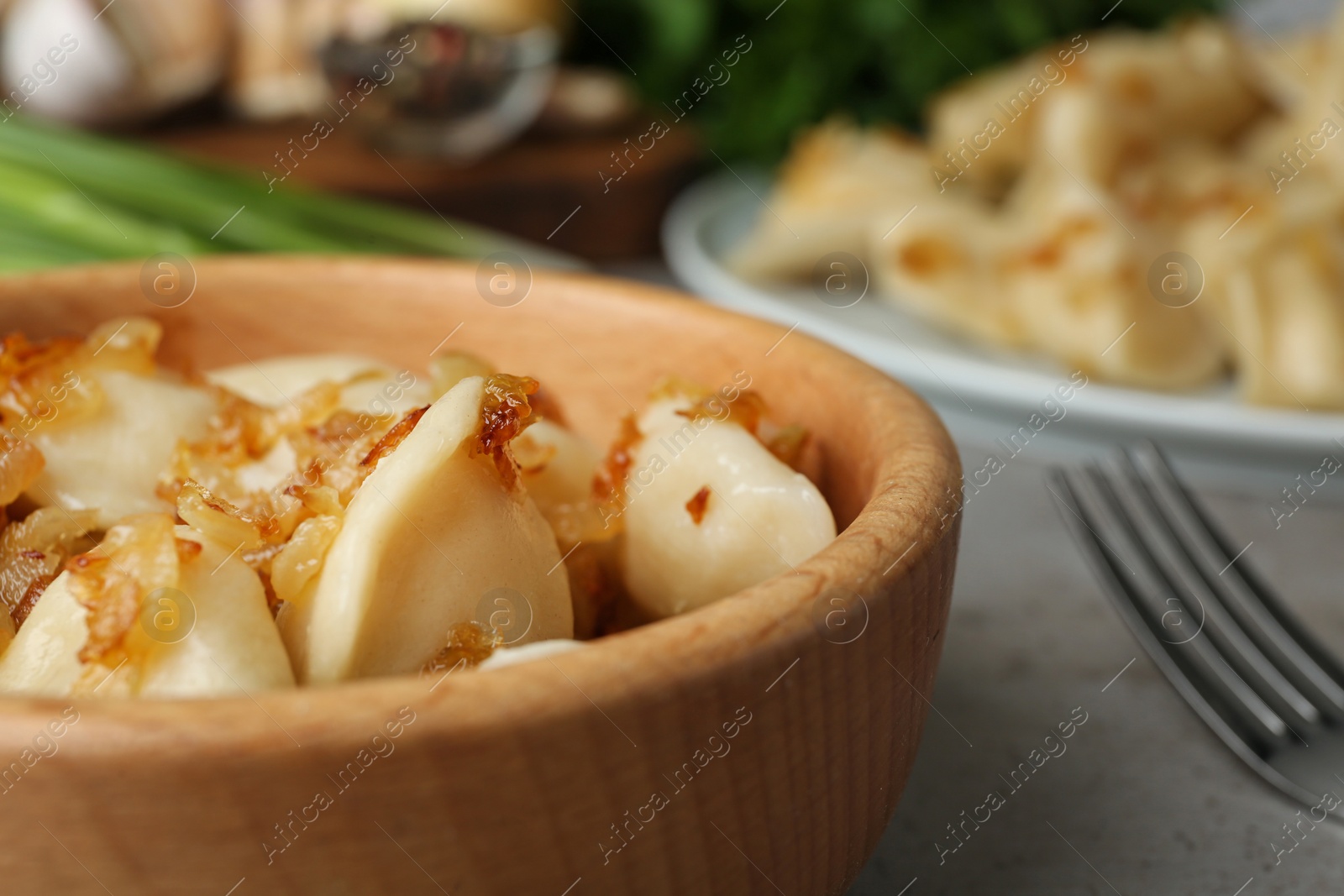 Photo of Delicious cooked dumplings with fried onion on grey table, closeup