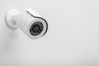 Photo of Modern CCTV security camera on white wall. Space for text