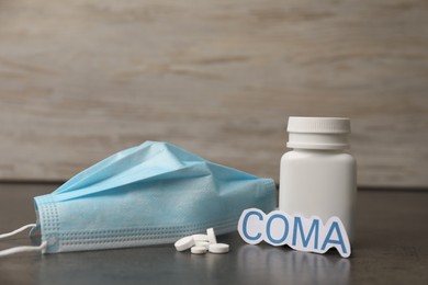 Photo of Word Coma with bottle of pills and medical mask on grey table
