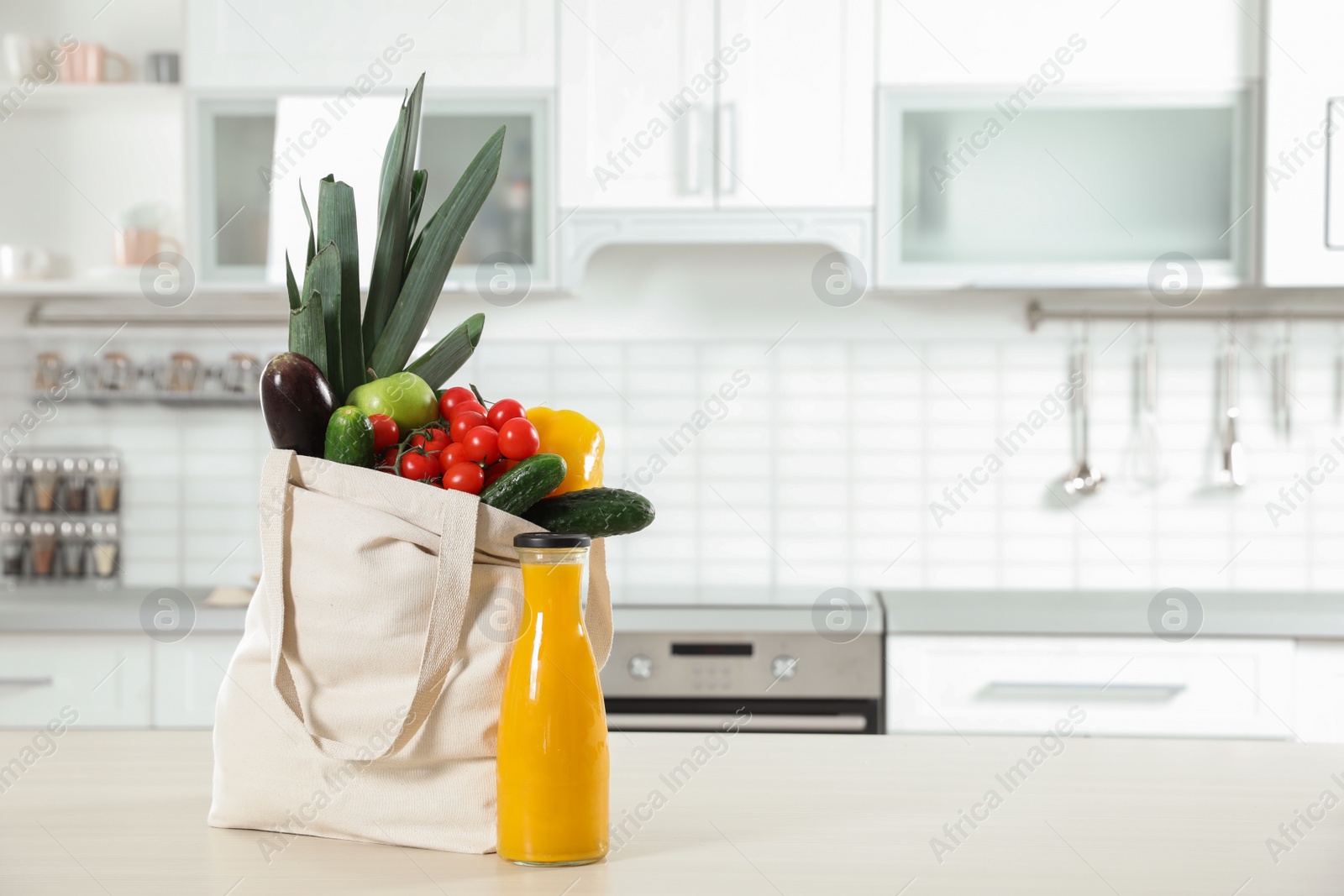 Photo of Textile shopping bag full of vegetables and juice on table in kitchen. Space for text