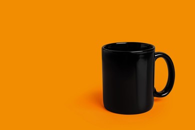 Photo of One black ceramic mug on orange background, space for text