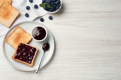 Photo of Toasts and blueberry jam served on white wooden table, flat lay. Space for text