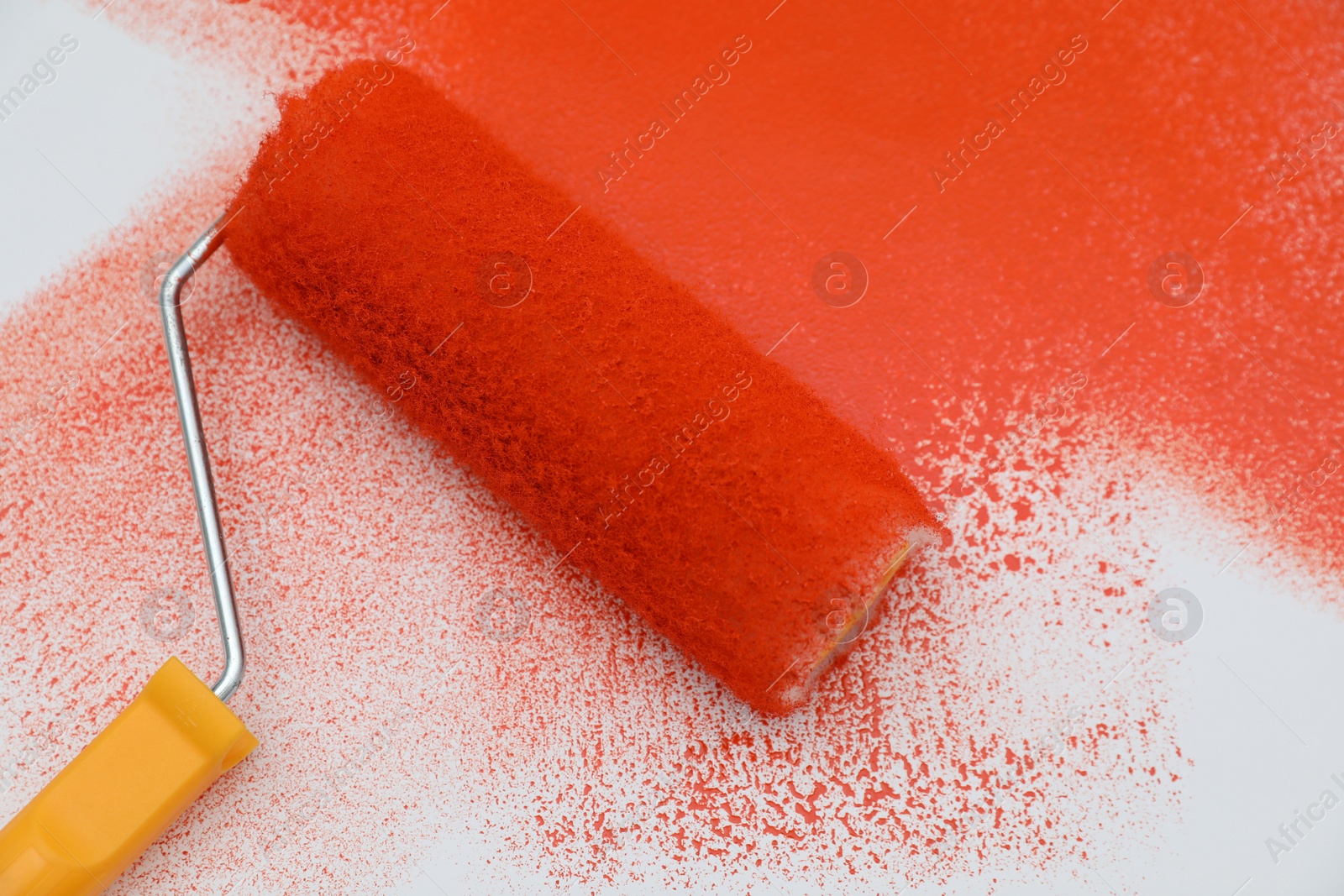 Photo of Roller brush and strokes of orange paint on white background, closeup