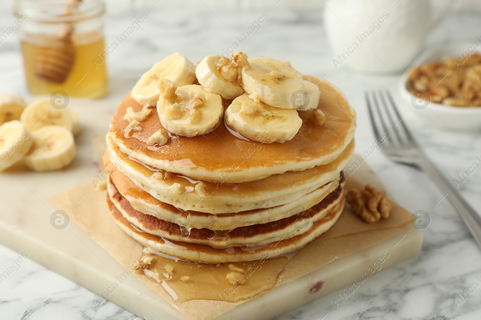 Photo of Delicious pancakes with bananas, walnuts and honey on white marble table, closeup